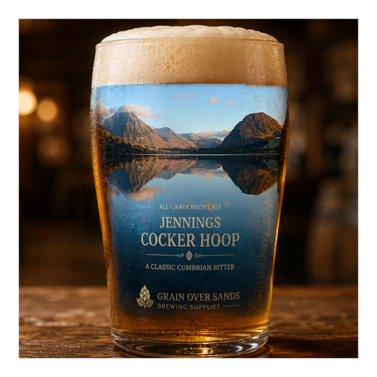 A pint glass of beer with a printed scenic label reading 'Jennings Cocker Hoop' and 'Grain Over Sands Brewing Supplies,' standing on a wooden table in a dimly lit pub setting.